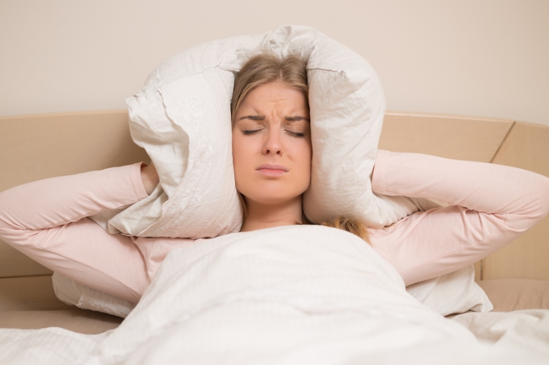 Angry woman disturbed with a noise trying to sleep and covering her ears with a pillow.