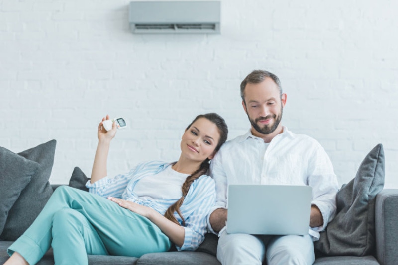 Going Ductless. Couple on couch with ductless air conditioning unit on wall.