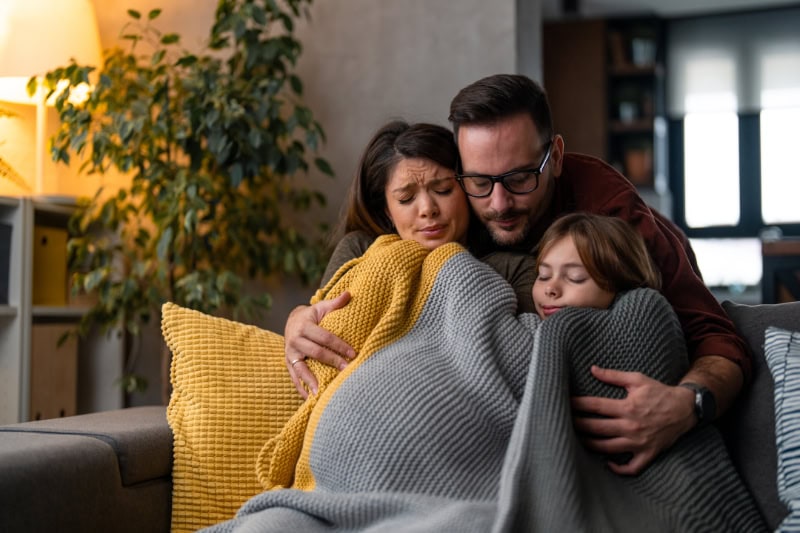 Why Isn’t My Furnace Heating My Entire Home? Family of three huddled under a blanket to stay warm in their home.