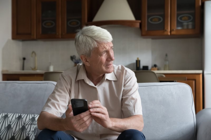 What’s That Smell Coming From My Furnace? Photo of a man on his phone, looking out a window seemingly concerned.