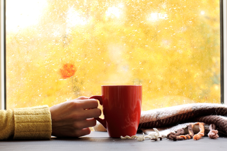 red mug of hot drink, when behind a window is rain in autumn