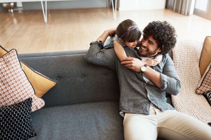 Father and daughter laughing on couch.