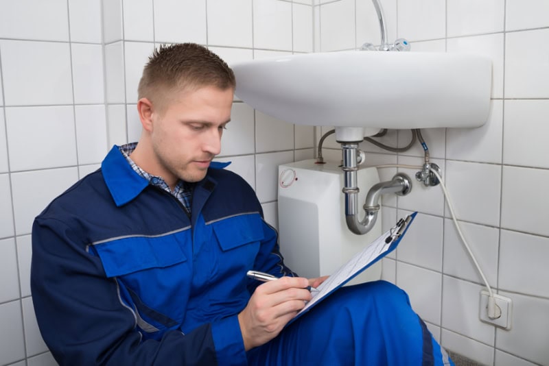 When was the last time you thought about your plumbing? If you’re like most Huntertown homeowners, it’s probably only when something goes wrong—a leaky faucet, a clogged drain, or worse, a burst pipe. Photo of a plumber sitting next to a bathroom sink performing maintenance.
