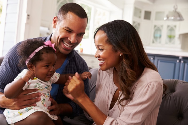 Why Get a Water Filtration System? Photo of a mother and father playing with their baby girl in their living room.