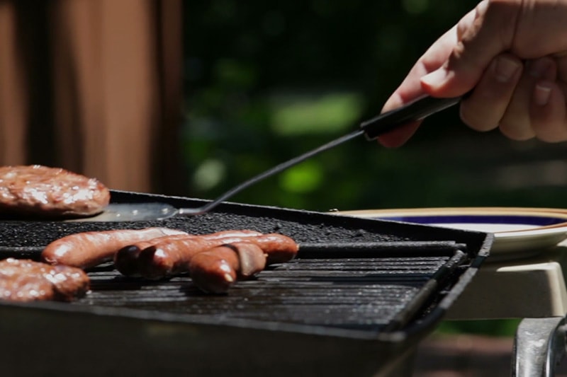 Photo of hot dogs being cooked on a grill outdoors.
