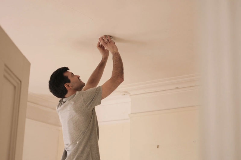 How Often Do I Need to Replace the Batteries in My Smoke and CO Detectors? Man changing smoke detector batteries.